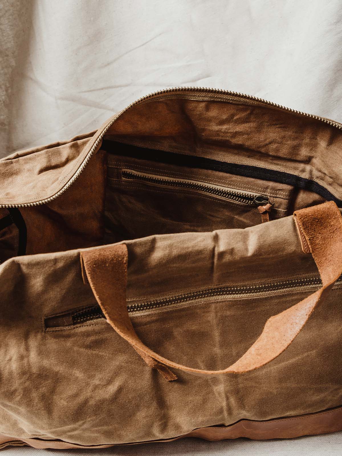 Details of tan weekender bag's internal and external zipper for additional storage.