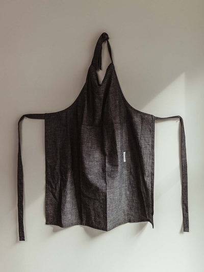 Grey kitchen apron hangin on the wallCloth dark grey apron hanging on white wall