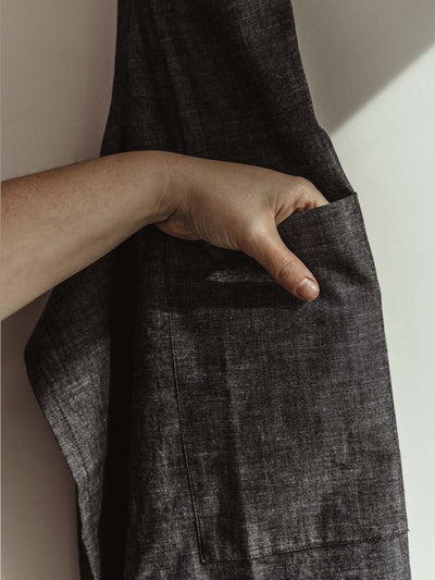 Hand reaching in the pocket of the gray apron hanging on the wall in a kitchen