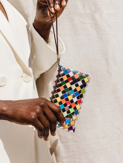 Female model holding multi-colored up cycled clutch on white background in a white outfit.