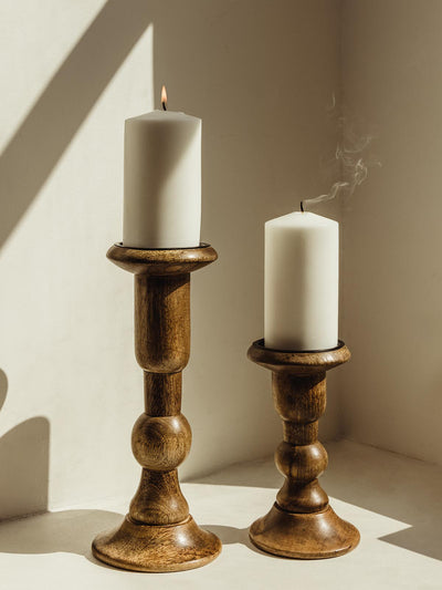 Wooden candle holders; one large and one small. Holder hold white candle on a white table. 