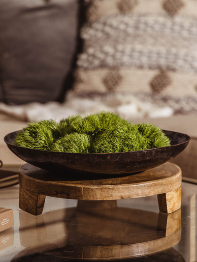 Wooden footed tray on glass table with metal bowl and greenery placed on tray.