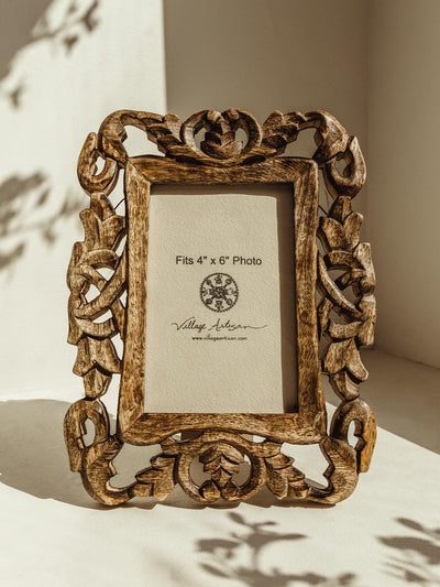 Wooden picture frame with carved details on a white table. 