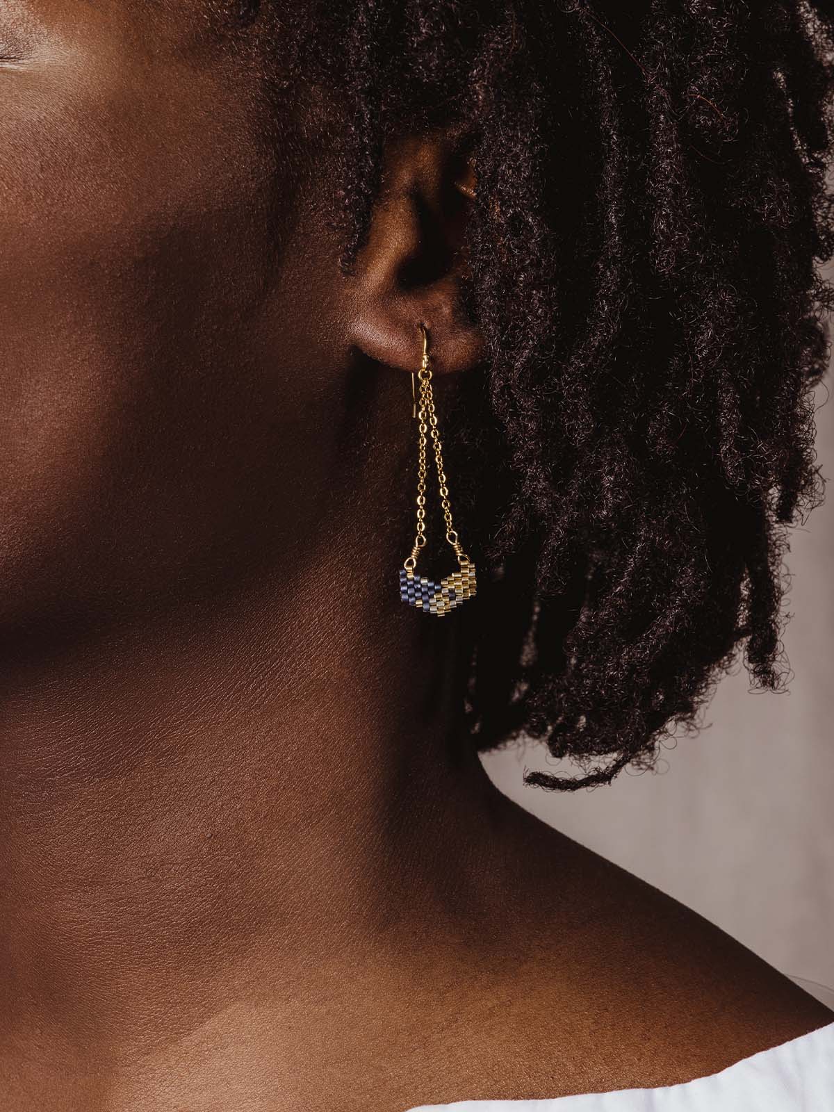 Model wearing gold and blue earrings with beaded pendants