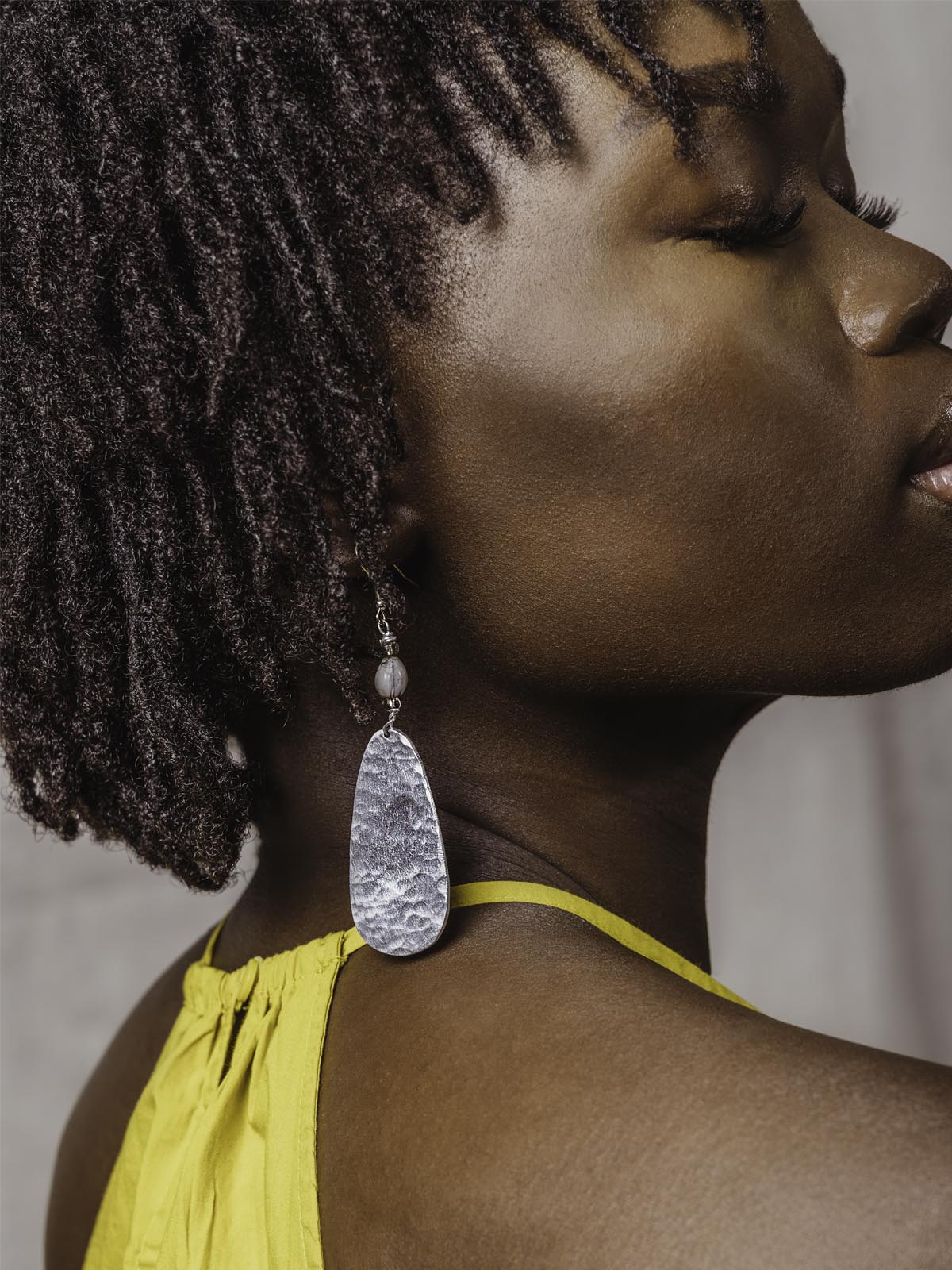 close up of Aluminum earrings on model in a yellow top closing her eyes