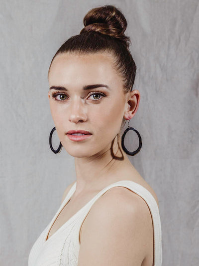 Model wearing horn Hoop Earrings. Large hoop shape with  black, brown, and white color tones