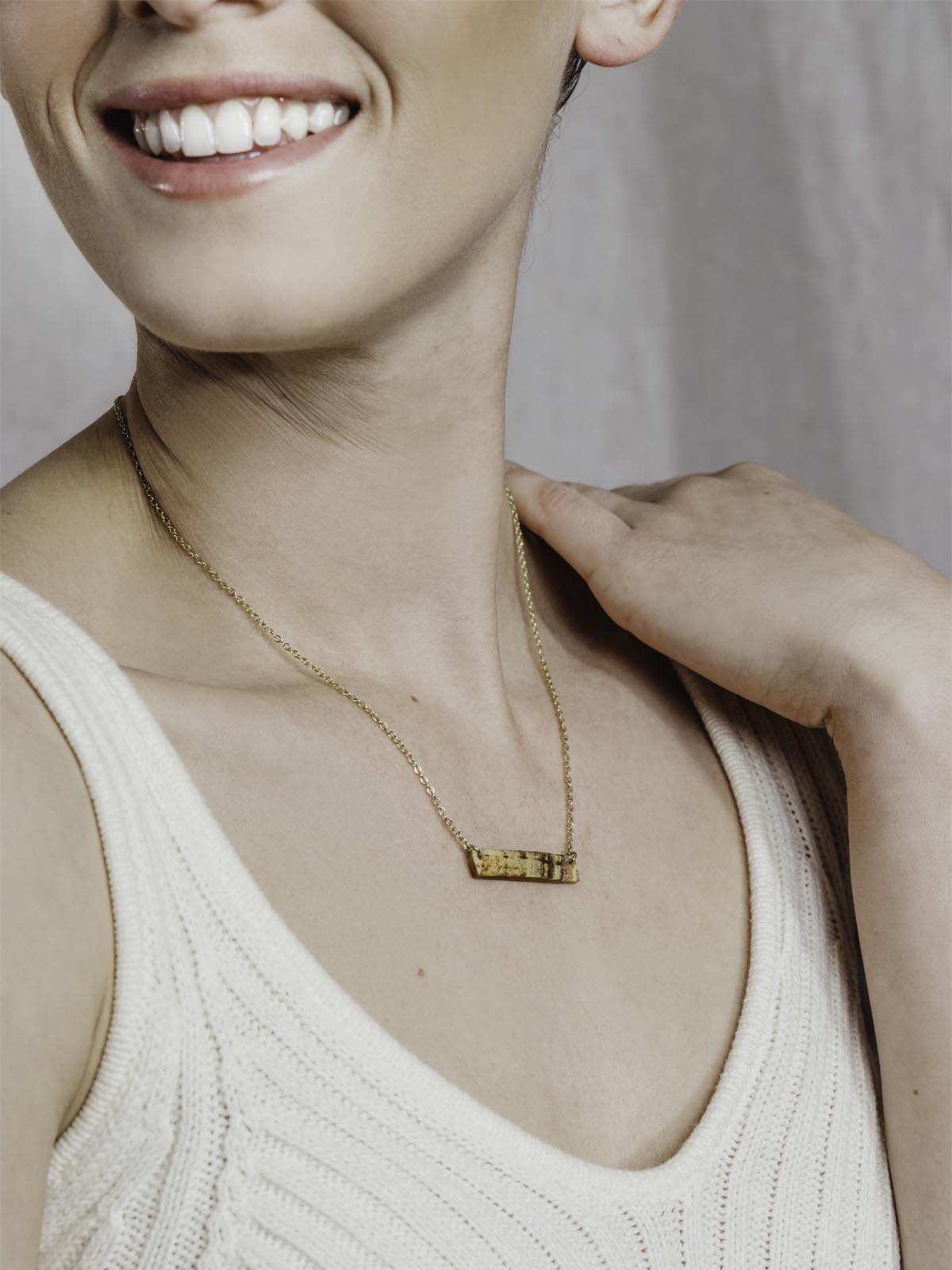 Mode wearing Medium length necklace with gold chain on a white background with small rectangle textured pendant.