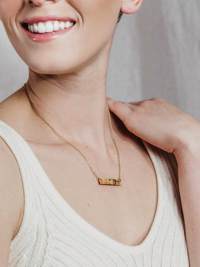 Mode wearing Medium length necklace with gold chain on a white background with small rectangle textured pendant.