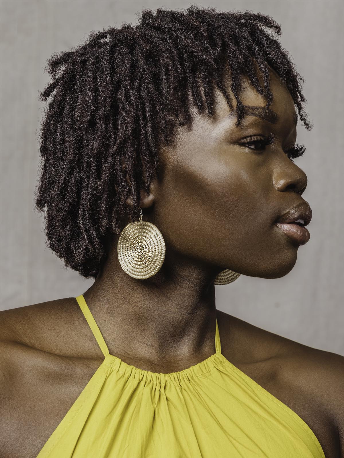 Tan circle earrings on a female wearing a yellow top. 