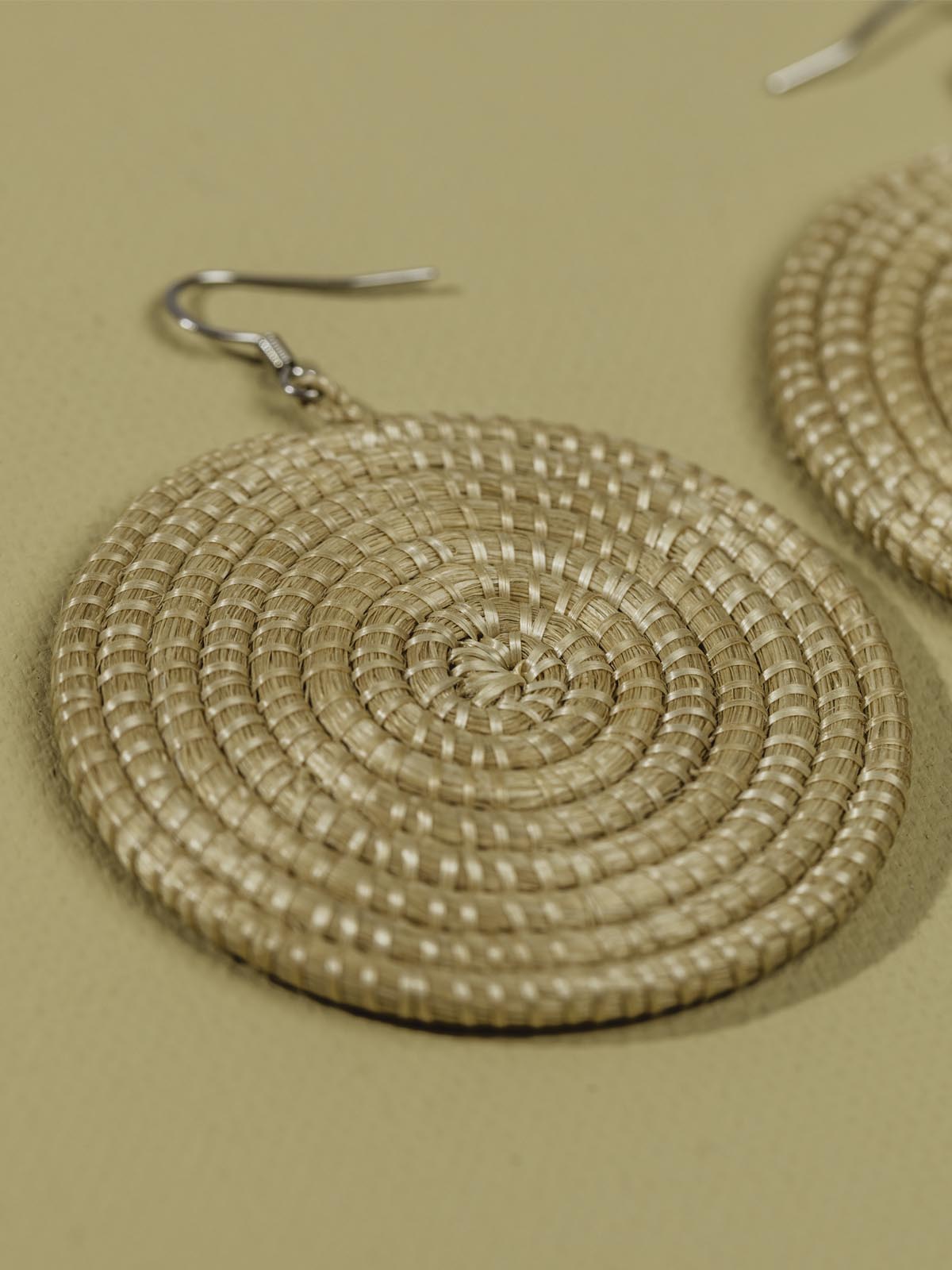 Tan woven earrings laying on a tan textured background. 