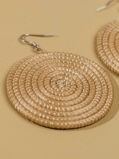 Tan woven earrings laying on a tan textured background. 