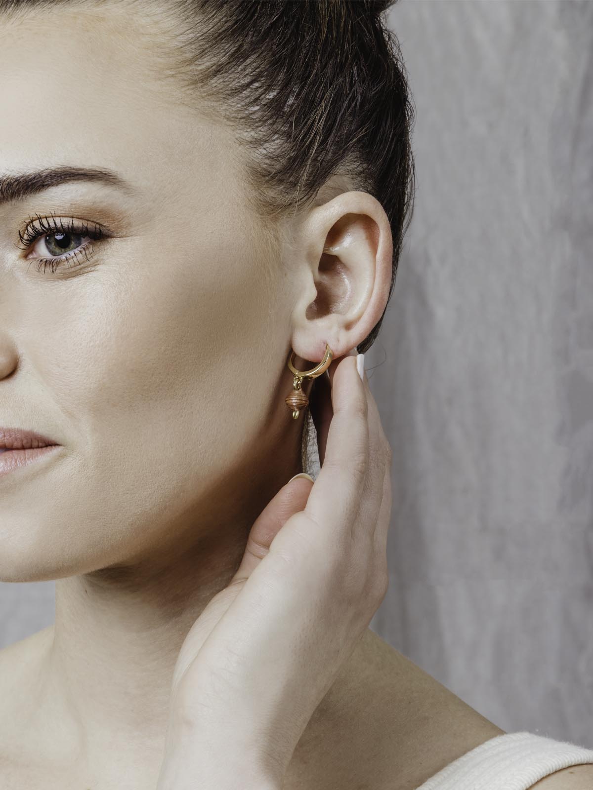 Model gold hoop earrings with brown bead charm.