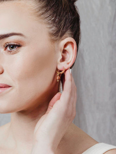 Model gold hoop earrings with brown bead charm.