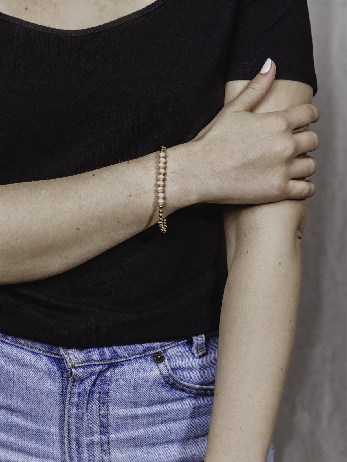 Model wearing golden beaded bracelet with nine peach beads