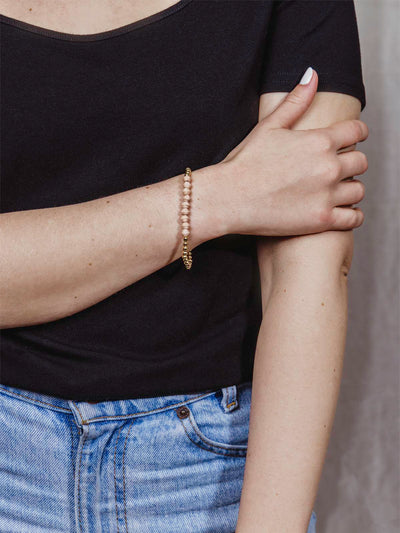 Model wearing golden beaded bracelet with nine peach beads