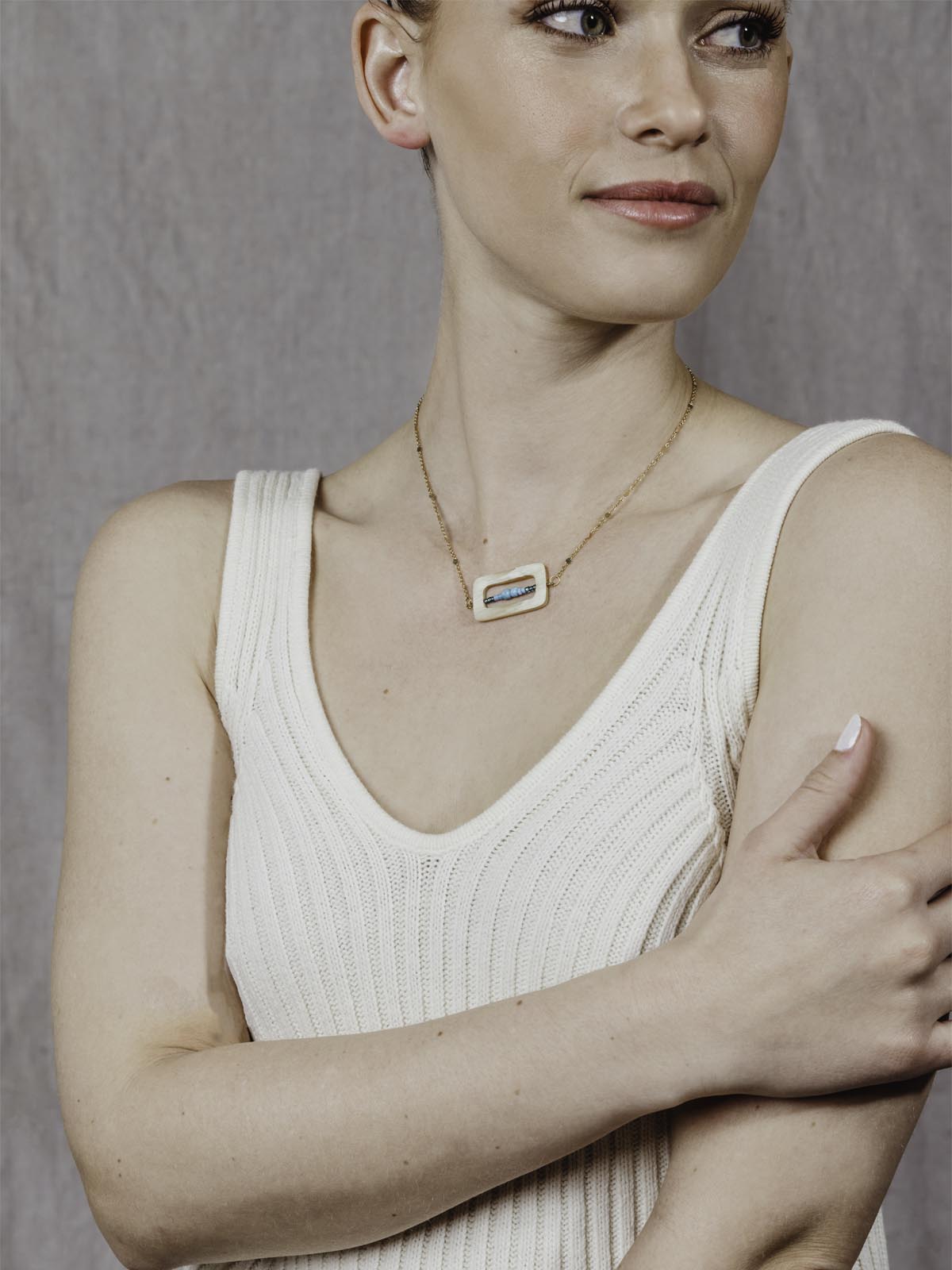 model wearing golden chain with details in the chain. Rectangulat pendant with turquoise beads in the middle of the rectangle shape. 