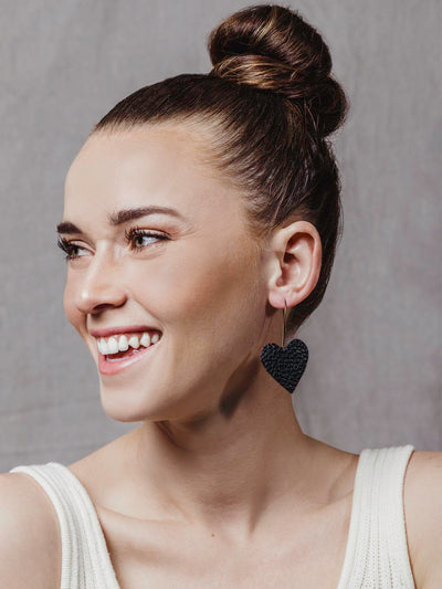 Model wearing black leather heart earrings.
