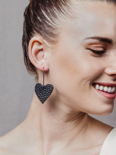 Close up of model wearing black leather heart earrings.
