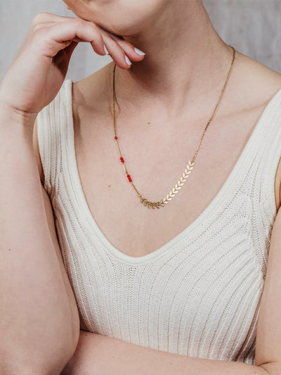 Model wearing golden chain necklace with arrow shapes and red beads