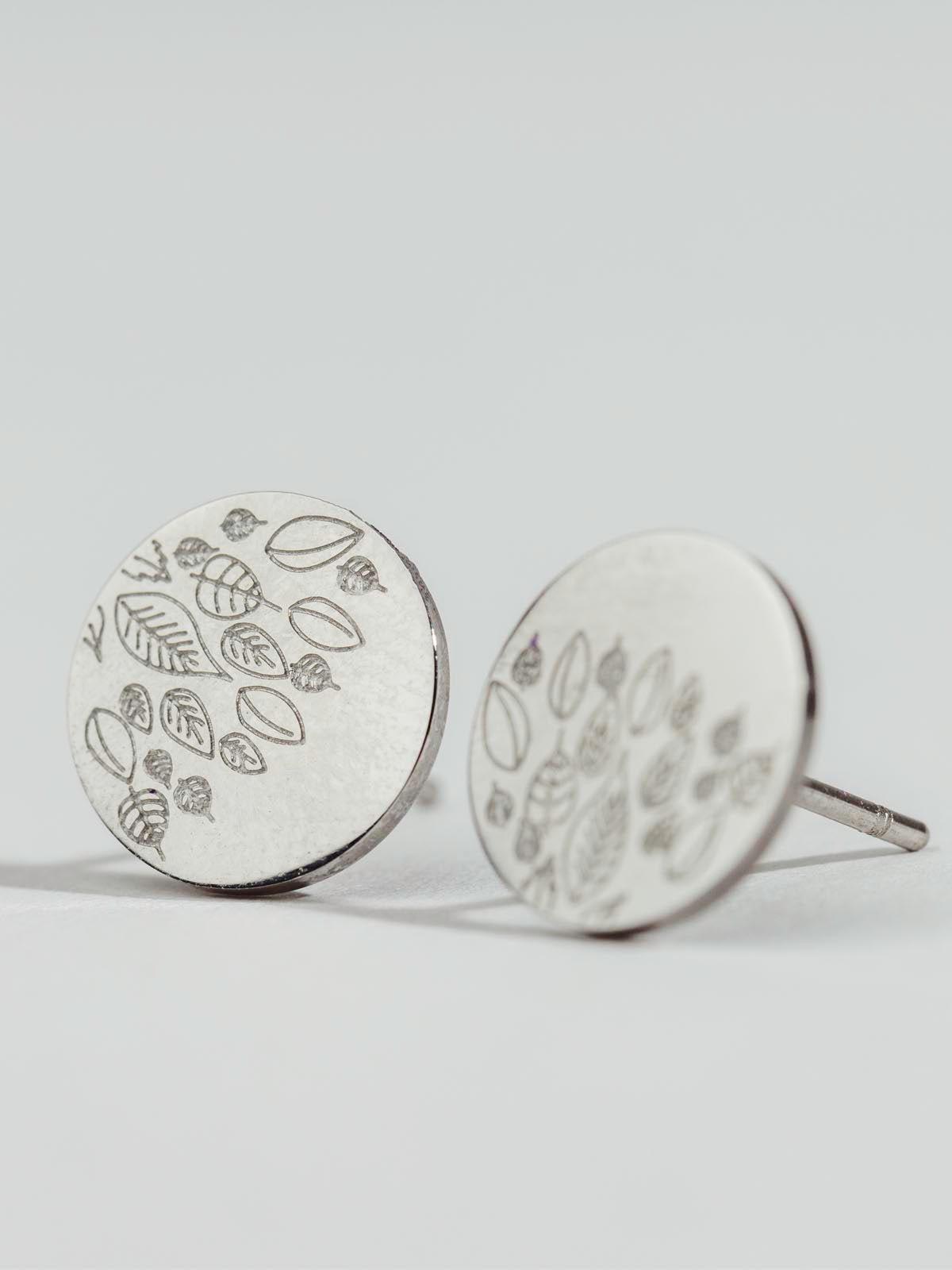 Silver studs with leave engravings sitting on white background. 