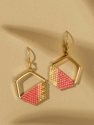 Pink and gold geometric earrings laying on a tan textured background. 