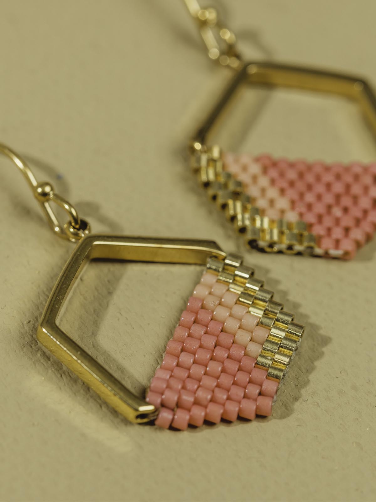 Pink and gold geometric earrings laying on a tan textured background. 
