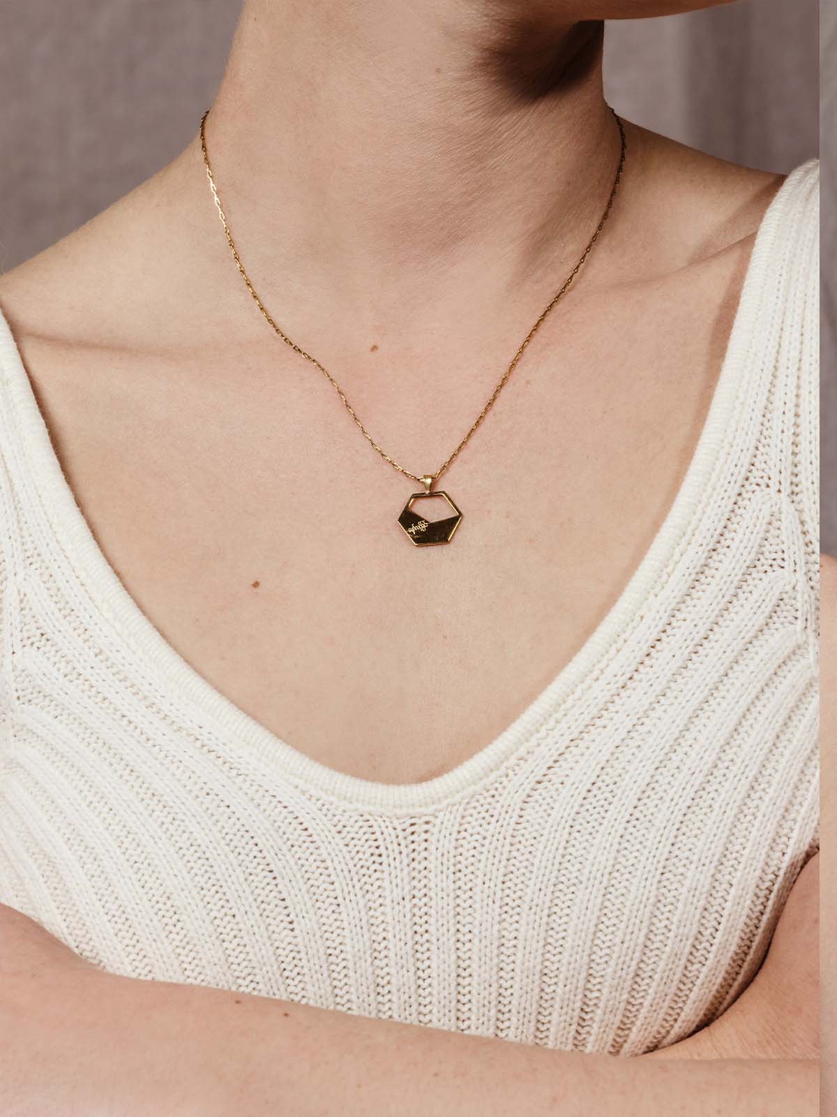 Geometric gold necklace on a model wearing white knit tank top. 