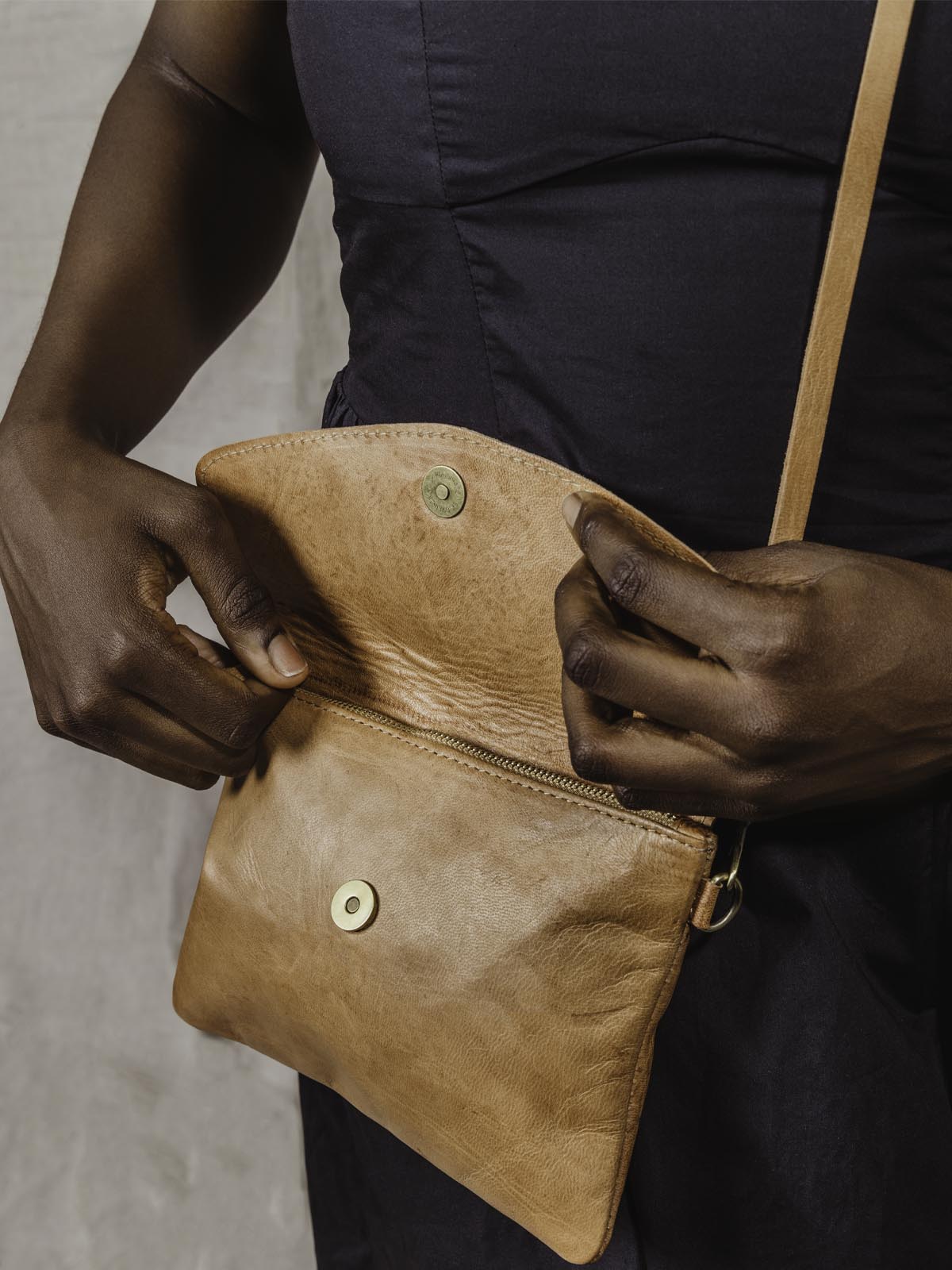 model opening the Brown Leather crossbody clutch on tan background