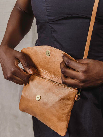 model opening the Brown Leather crossbody clutch on tan background