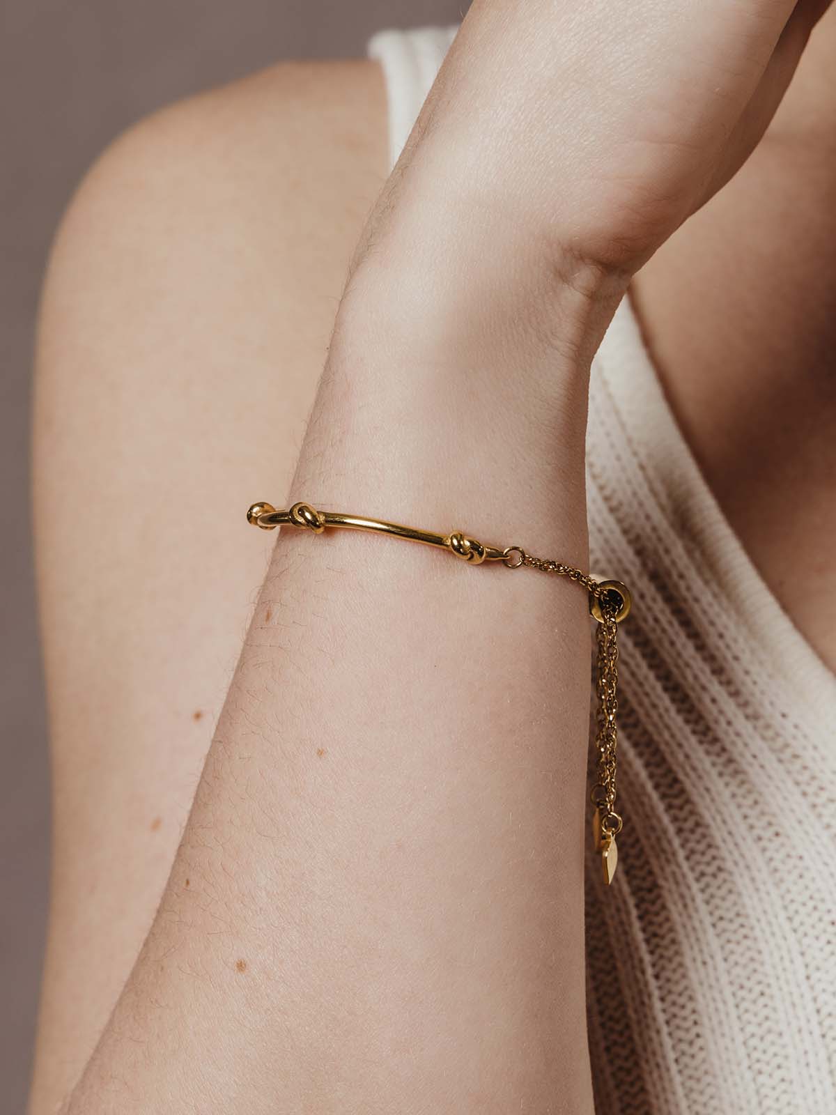 close up of model wearing gold knot bracelet with chain