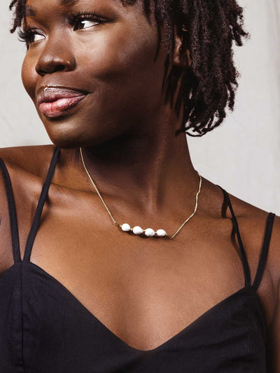Gold Necklace with four white beads on a model wearing a black shirt