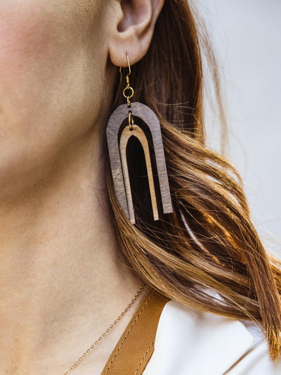 Wood earring on female model with dark brown arch shape layer over a light brown arch shape. Shapes are separate and move freely. 