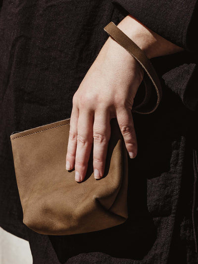 female model holding brown leather wristlet 