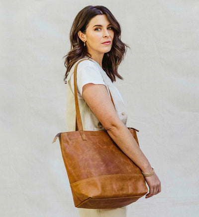 Woman standing sideways to the camera with a tan leather tote