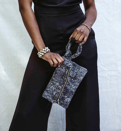 Women wearing a black jumpsuit while holding a nacy blue clutch and a neutral wrap bracelet
