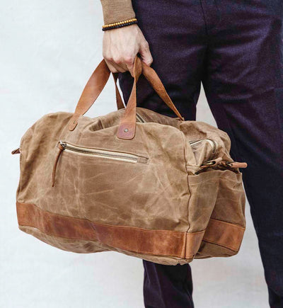 Tan canvas duffle bag with zipper being carried by a man with dark plans on 