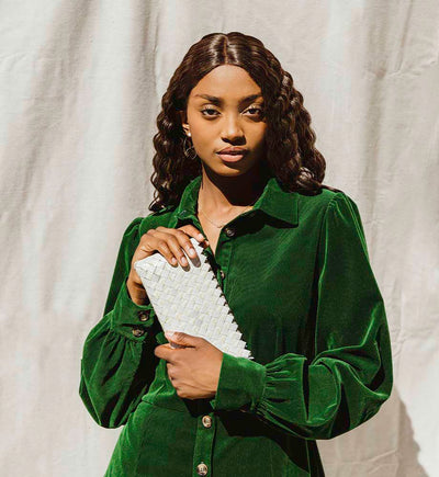 women with wavy hair holding a white upcycled clutch while wearing a green dress