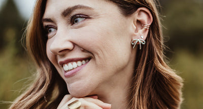 Women wearing gold bracelet, necklace and white and gold earrings in front of a white background