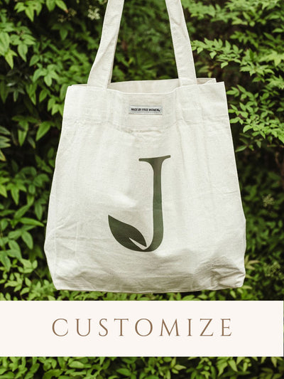 Canvas tote with customized logo. Tote is held infront of greenery. 