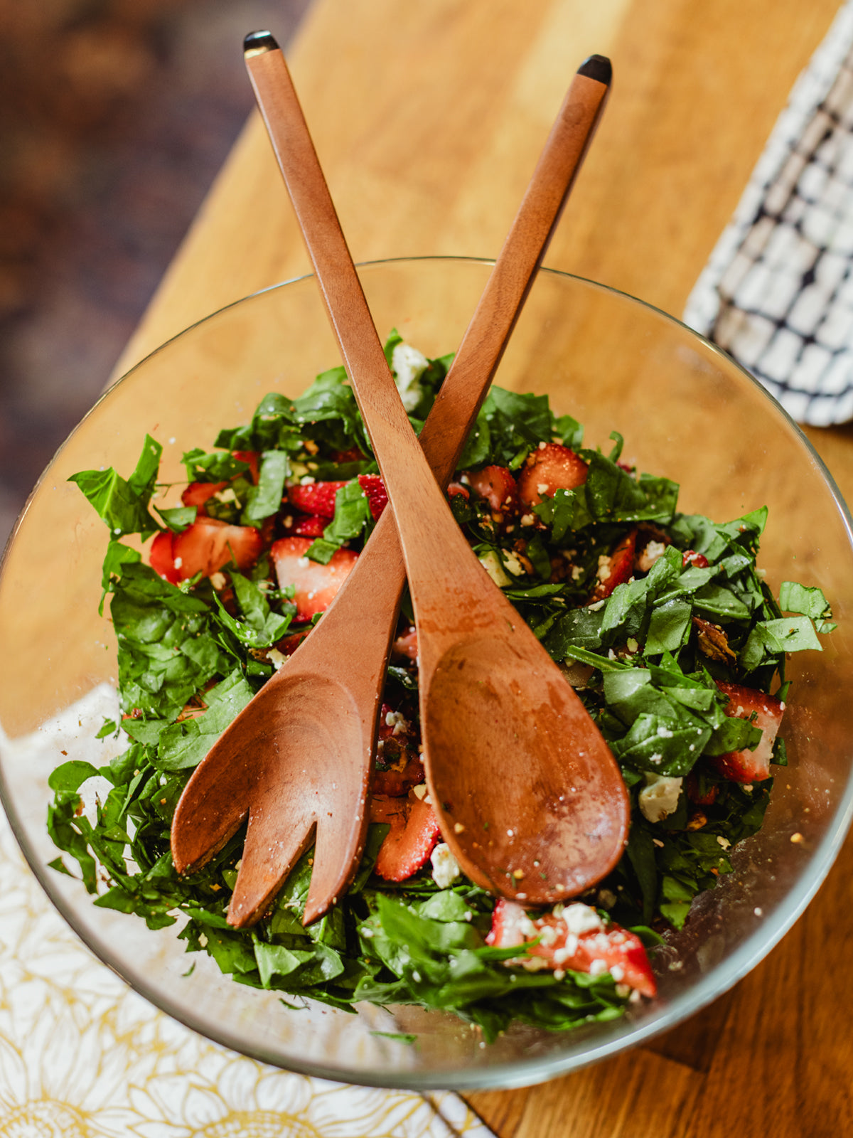 Brown wooden suzy salad servers in vibrant glass salad bowl on kitchen counter. 