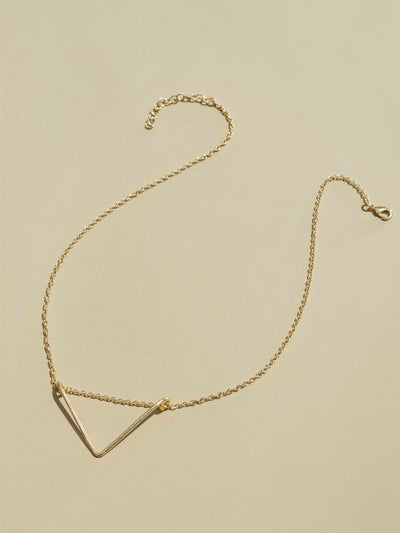 Crowned  free gold necklace with triangular shaped pendent on tan background.