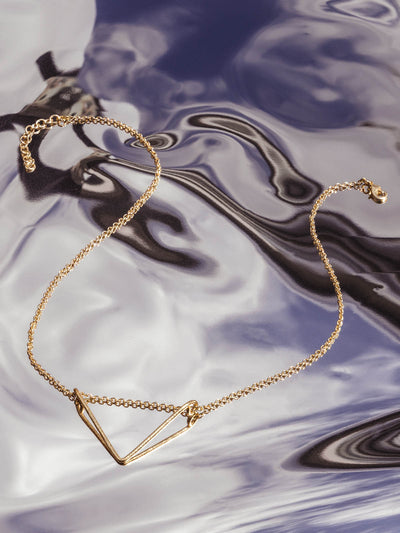 Crowned  free gold necklace with triangular shaped pendent on metallic background.