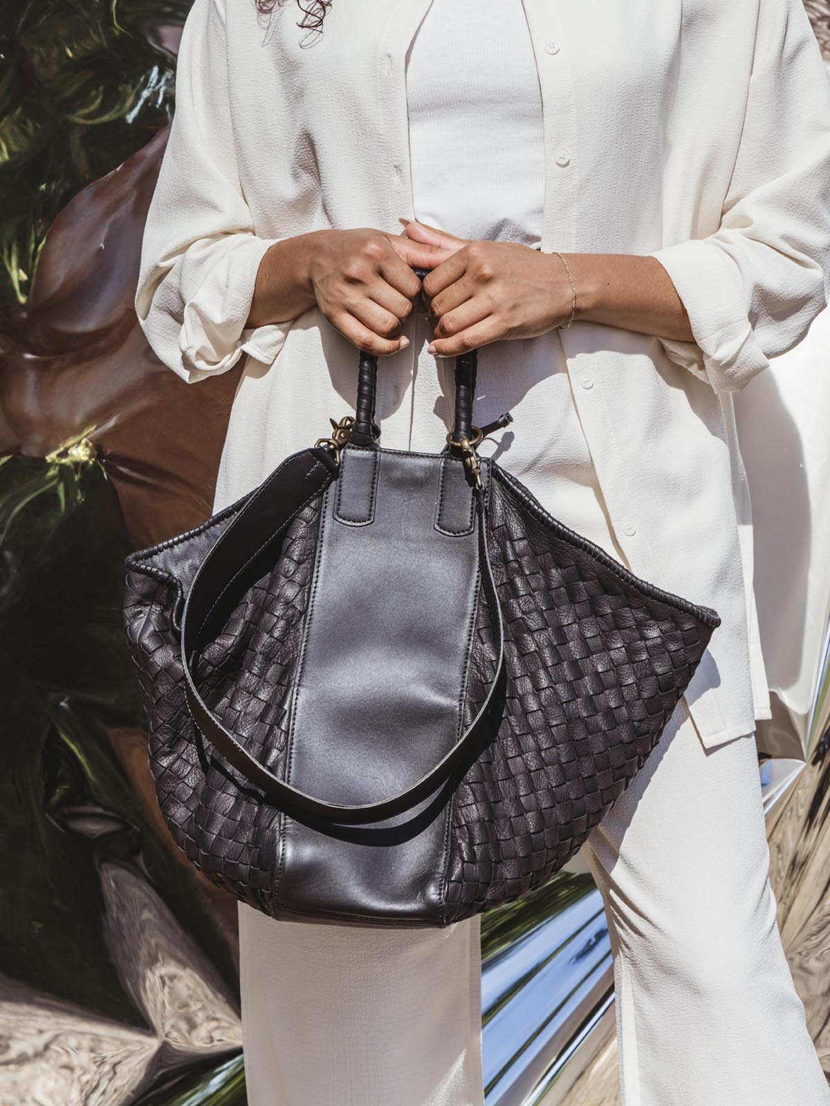 Model dressed in white top and pant holding Deux Mains leather all day tote bag.