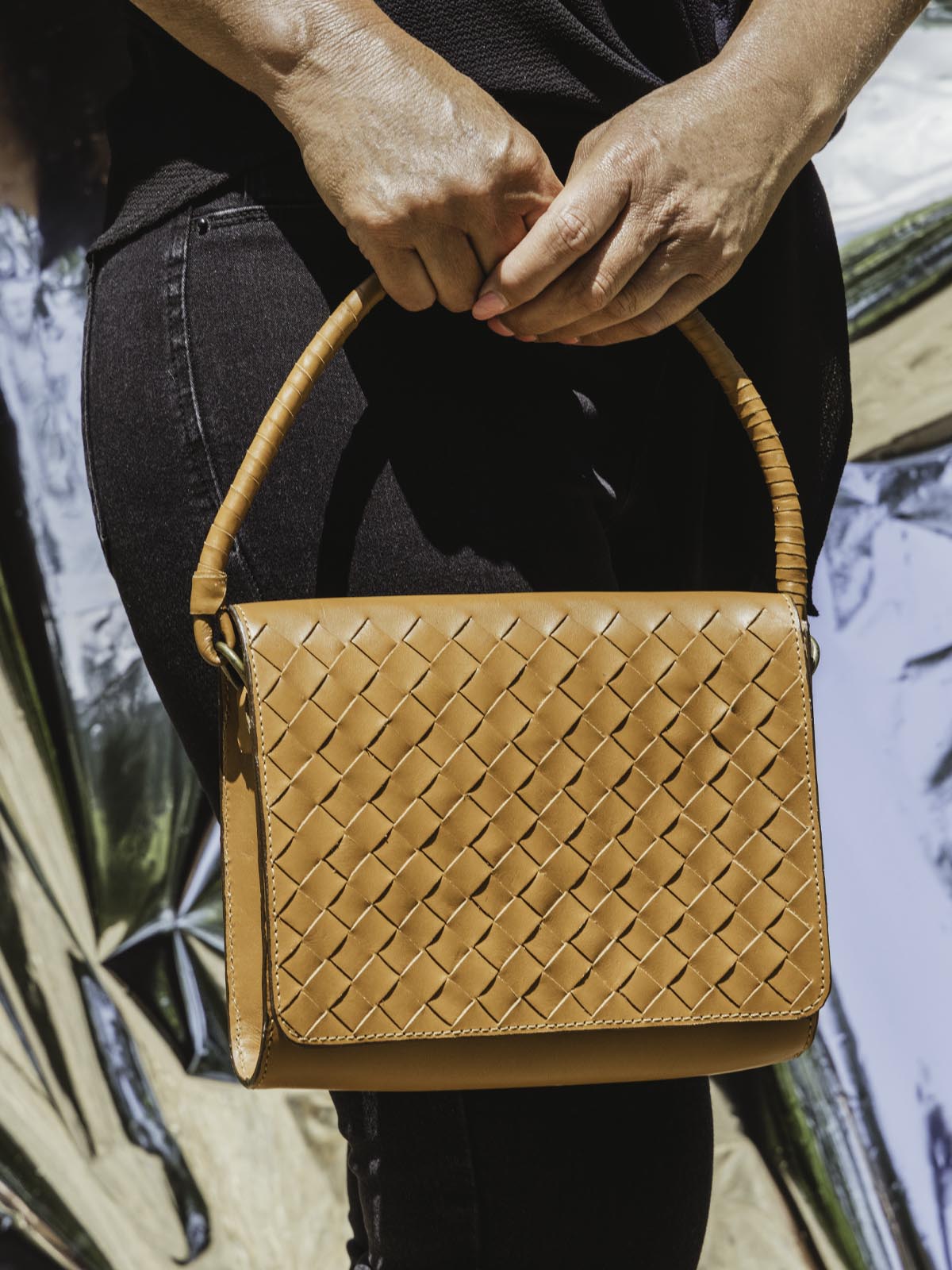 Model with handmade braided leather hand bag  holding it from clutch strap.
