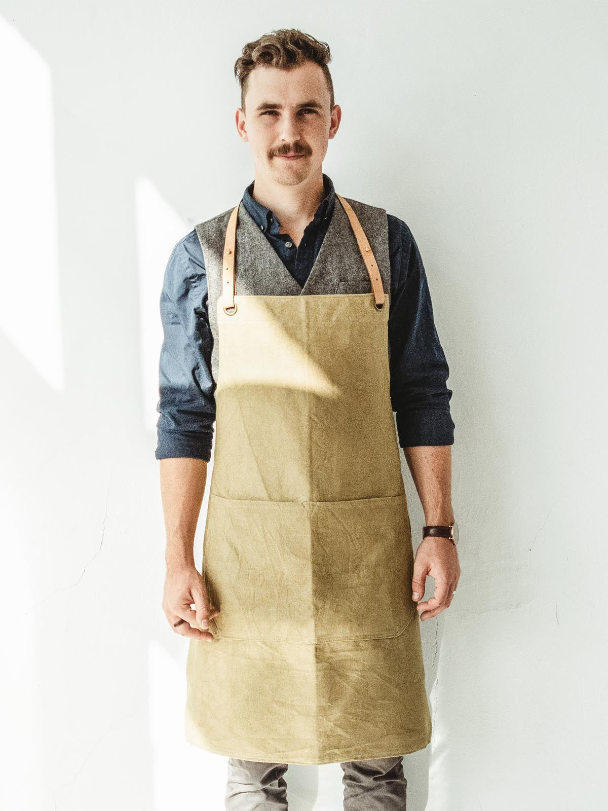 A man wearing a tan apron in from of a white wall