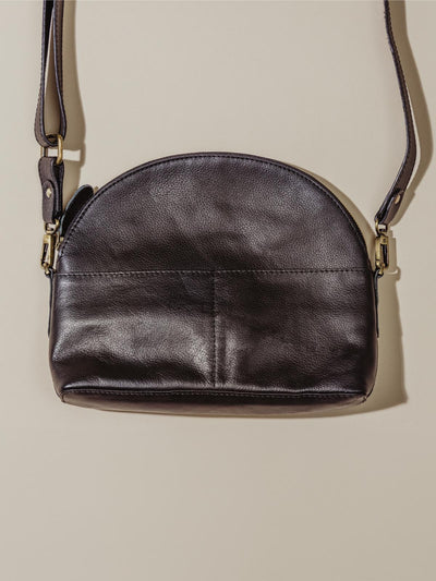 Black leather semi circle handbag laying on tan background. 