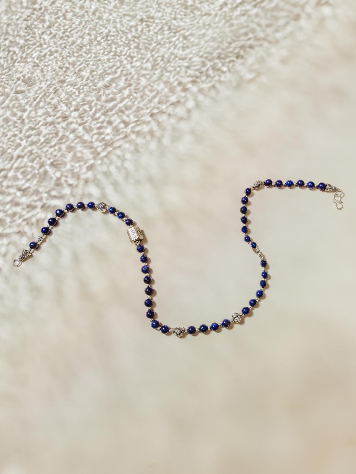 Blue and silver beaded necklace on white surface.