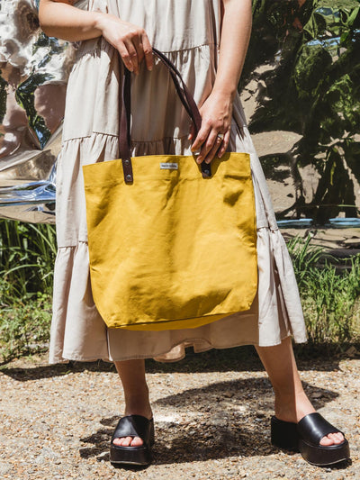 Model wearing a dress holding Made Free yellow tote in outdoor setting.