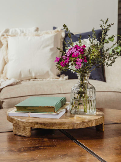 Large wood tray with books and flower vase atop while placed on a coffee table. 