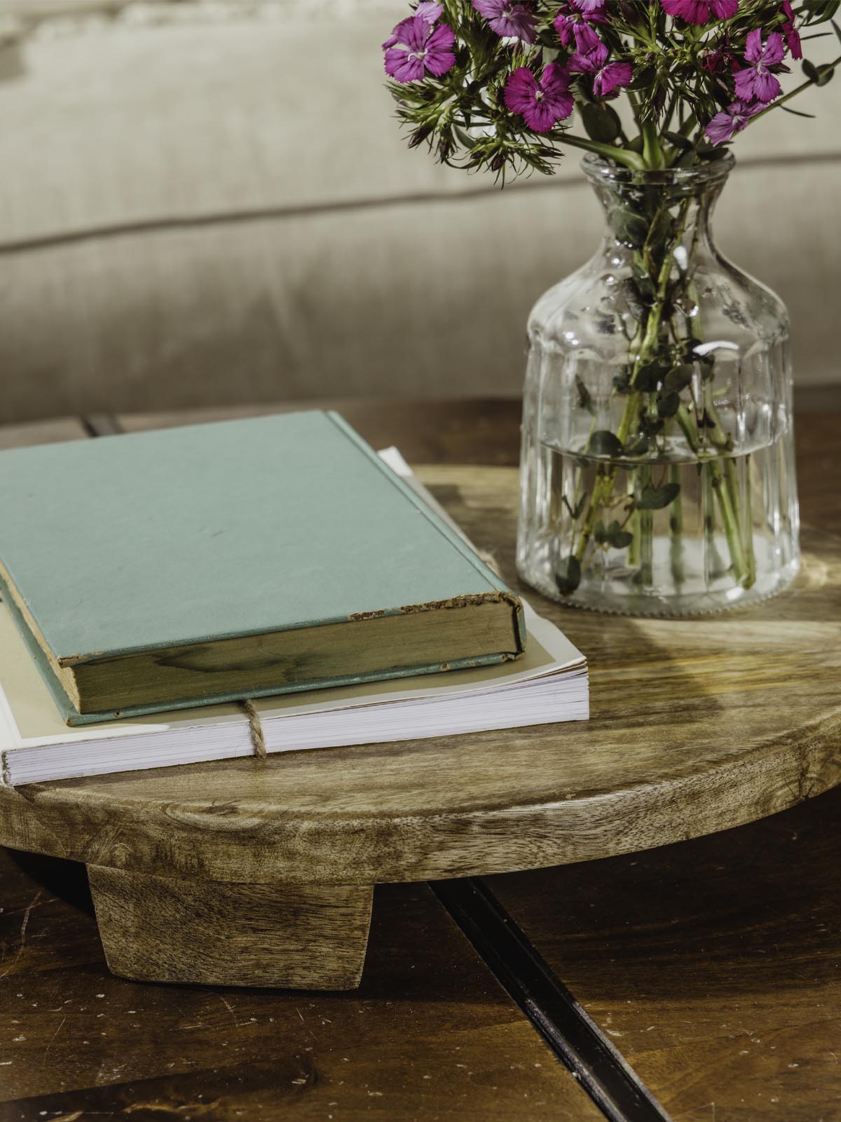 Closeup of large wood tray with books and flower vase atop while placed on a coffee table. 